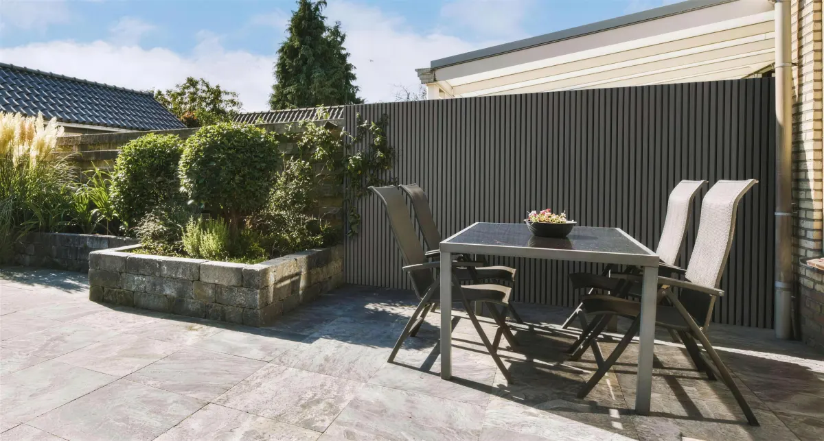 Terrasse mit grauer WPC Lamellenwand, Esstisch und Stühlen